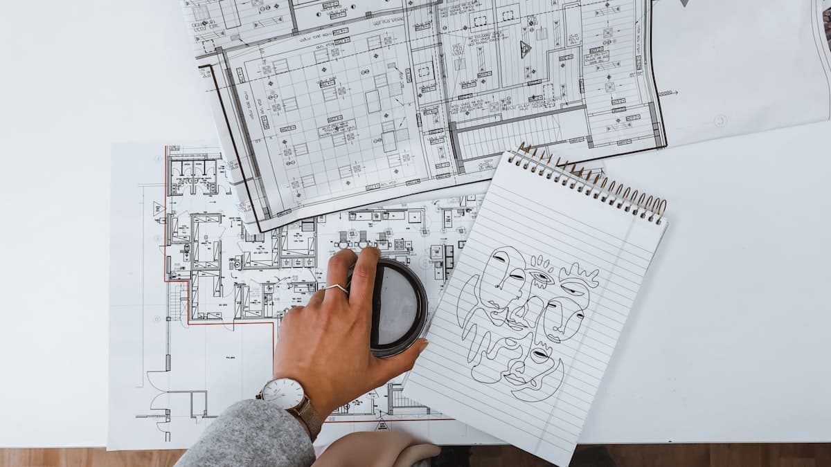 A hand with a magnifying glass examining construction blueprints