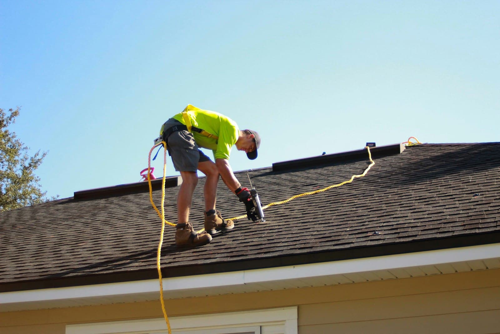 A roofer fastening shingles with a drill